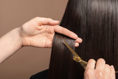 Photo of Hairdresser cutting client's hair with scissors on light brown background, closeup