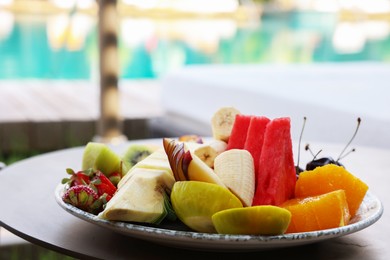 Photo of Plate with fresh fruits on table near sun lounger. Luxury resort with outdoor swimming pool