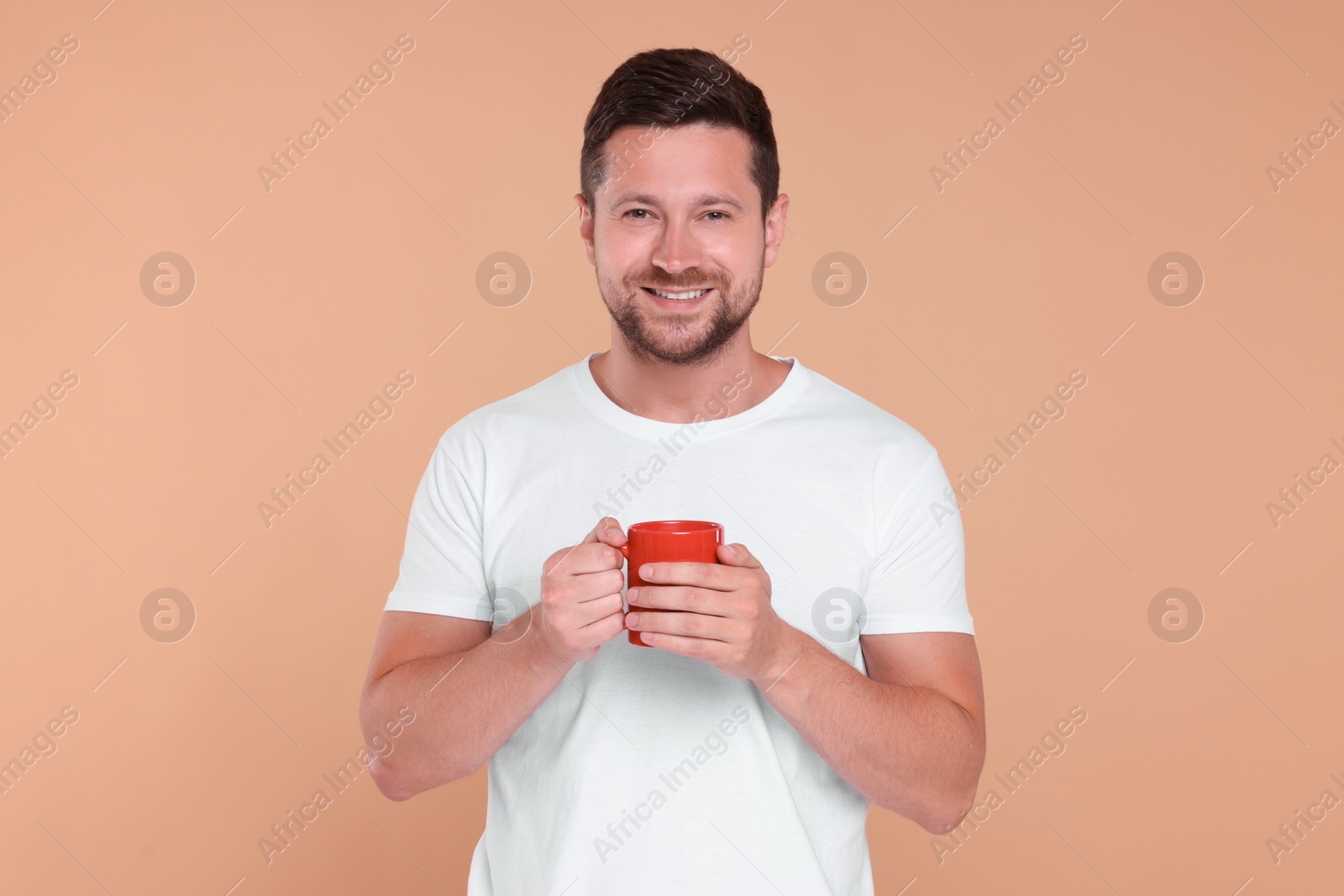 Photo of Portrait of happy man holding red mug on beige background