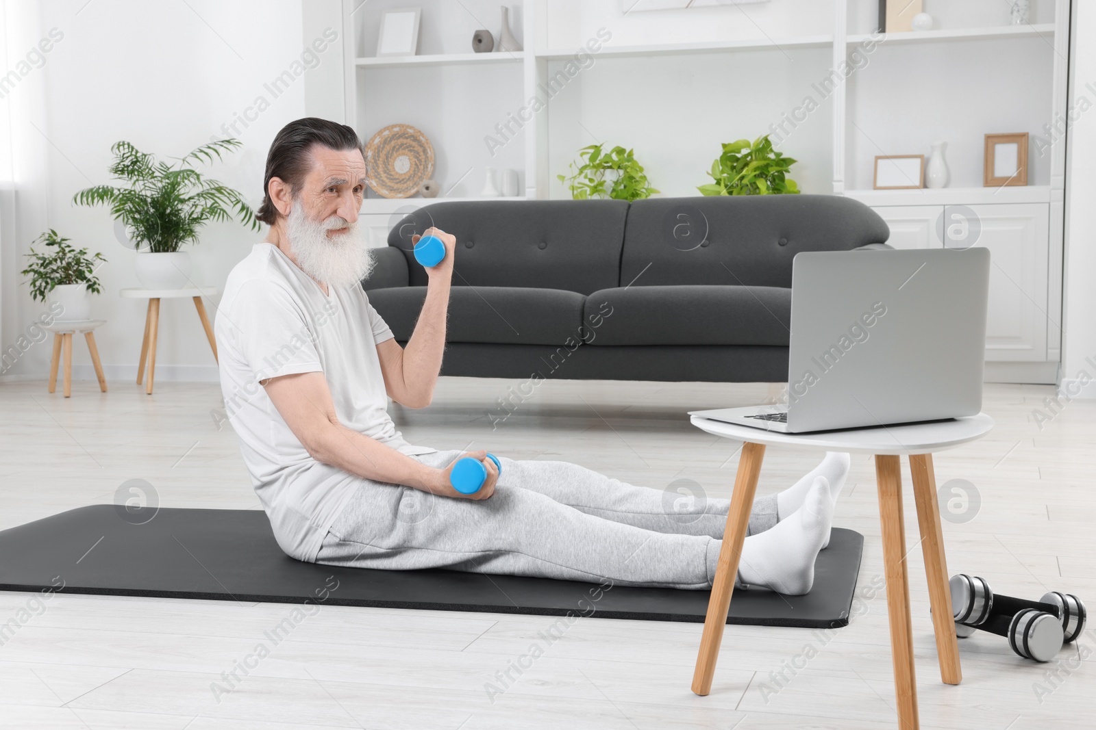 Photo of Senior man exercising with dumbbells while watching online tutorial at home. Sports equipment