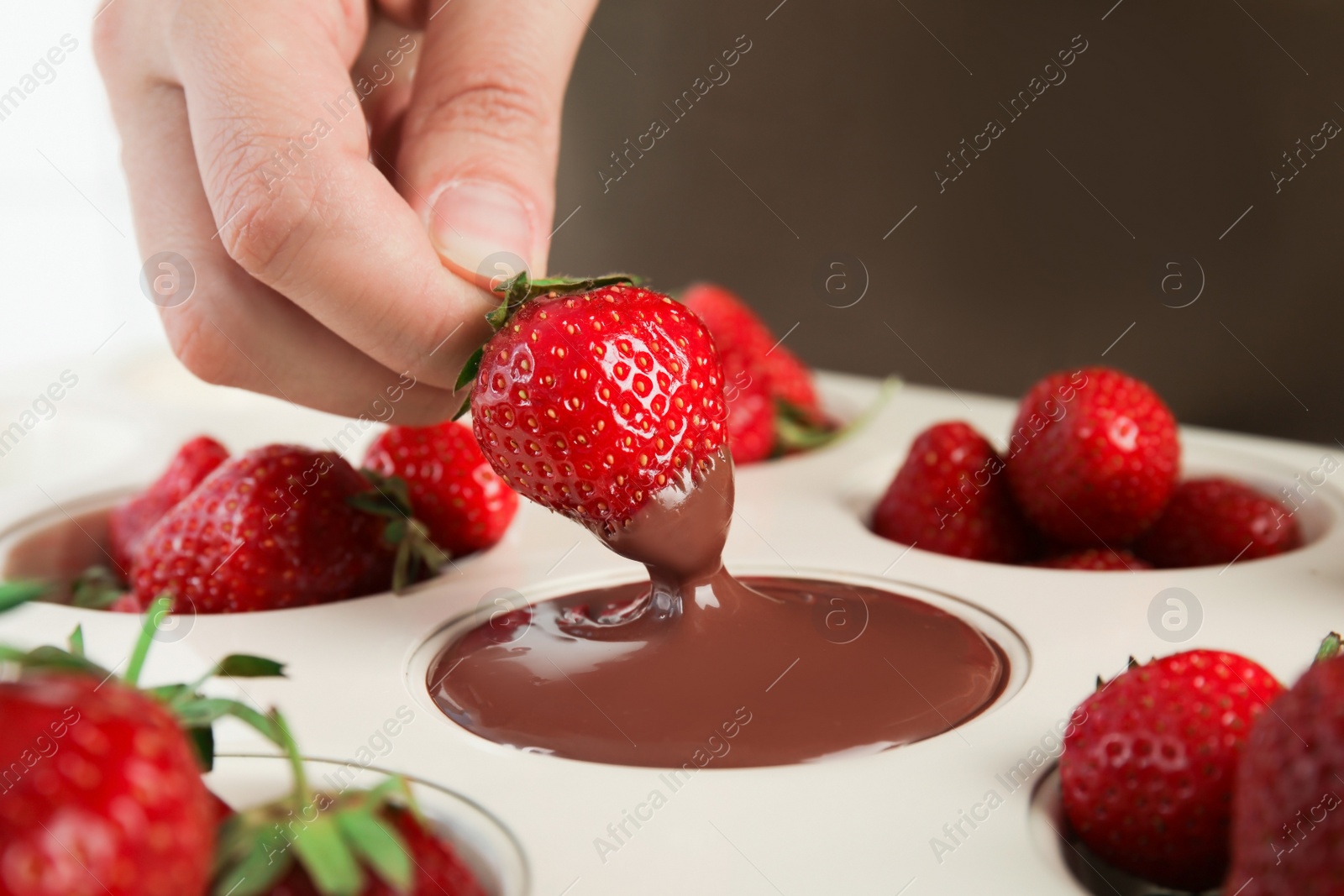 Photo of Woman dipping ripe strawberry into mold with melted chocolate, closeup