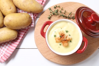 Photo of Tasty potato soup with croutons in ceramic pot and ingredients on white wooden table, flat lay