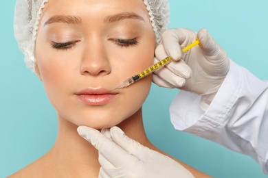 Young woman getting lips injection on color background, closeup. Cosmetic surgery