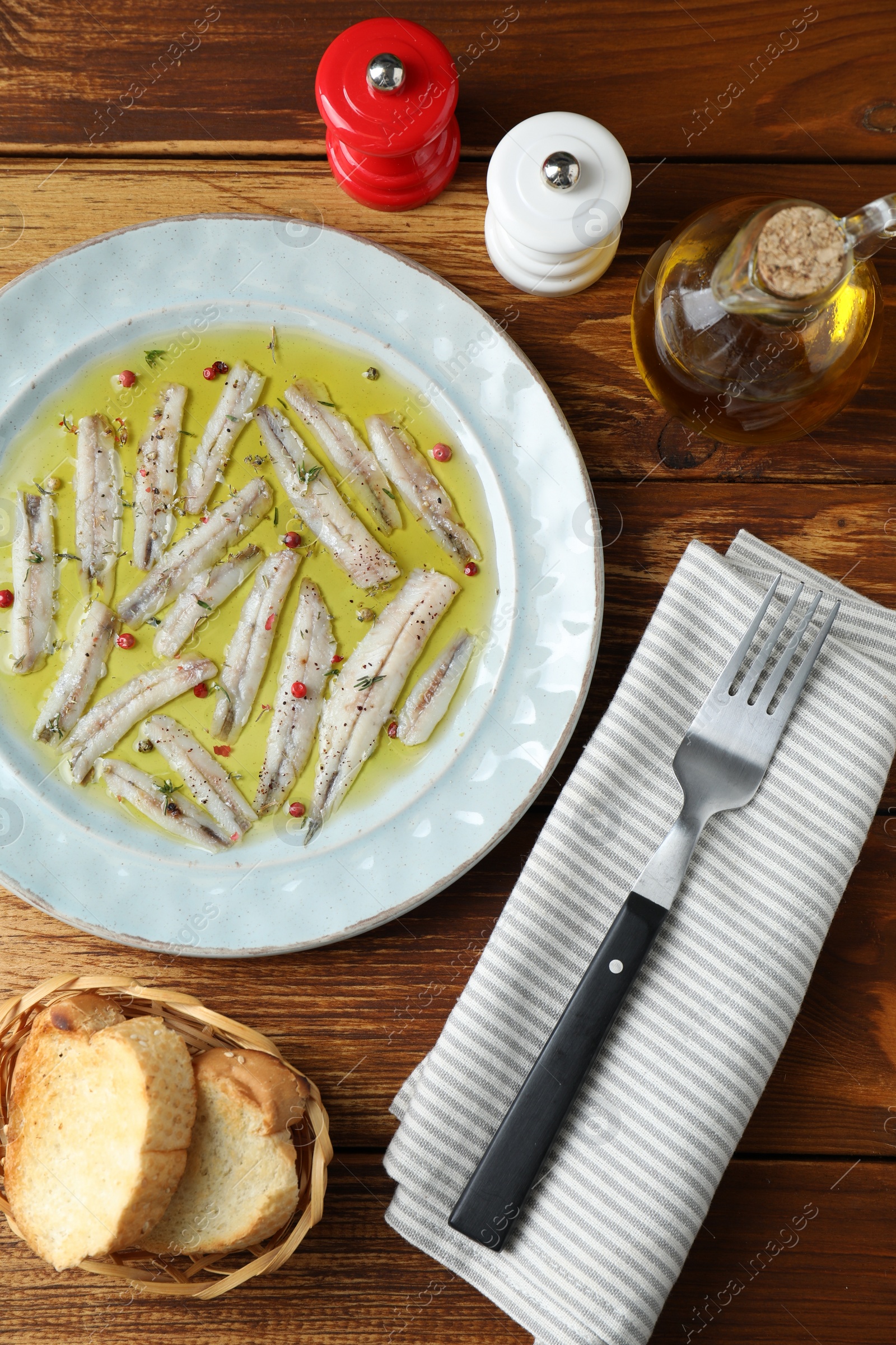 Photo of Tasty pickled anchovies with spices and products on wooden table, flat lay