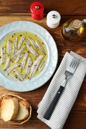 Tasty pickled anchovies with spices and products on wooden table, flat lay