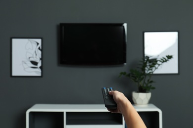 Photo of Woman switching channels on plasma TV with remote control at home