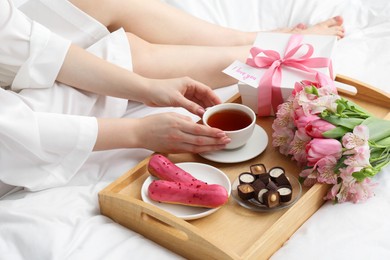 Photo of Tasty breakfast served in bed. Woman with tea, desserts, gift box, flowers and I Love You card at home, closeup