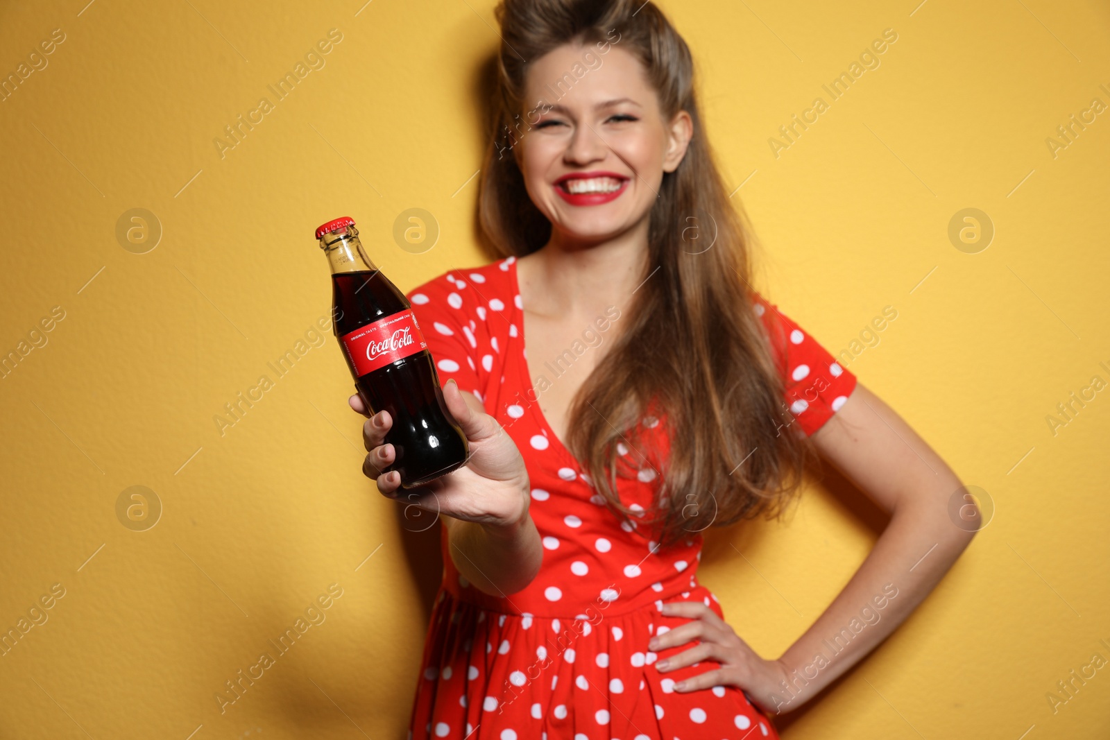 Photo of MYKOLAIV, UKRAINE - NOVEMBER 28, 2018: Young woman with bottle of Coca-Cola on color background