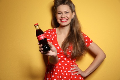 Photo of MYKOLAIV, UKRAINE - NOVEMBER 28, 2018: Young woman with bottle of Coca-Cola on color background