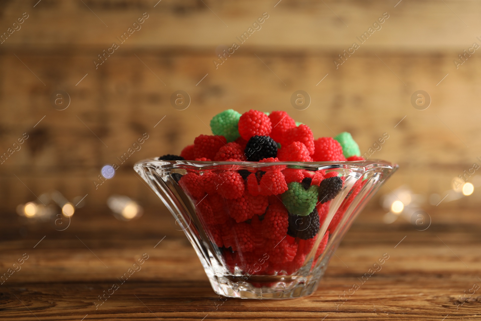 Photo of Delicious jelly candies in bowl on wooden table, closeup