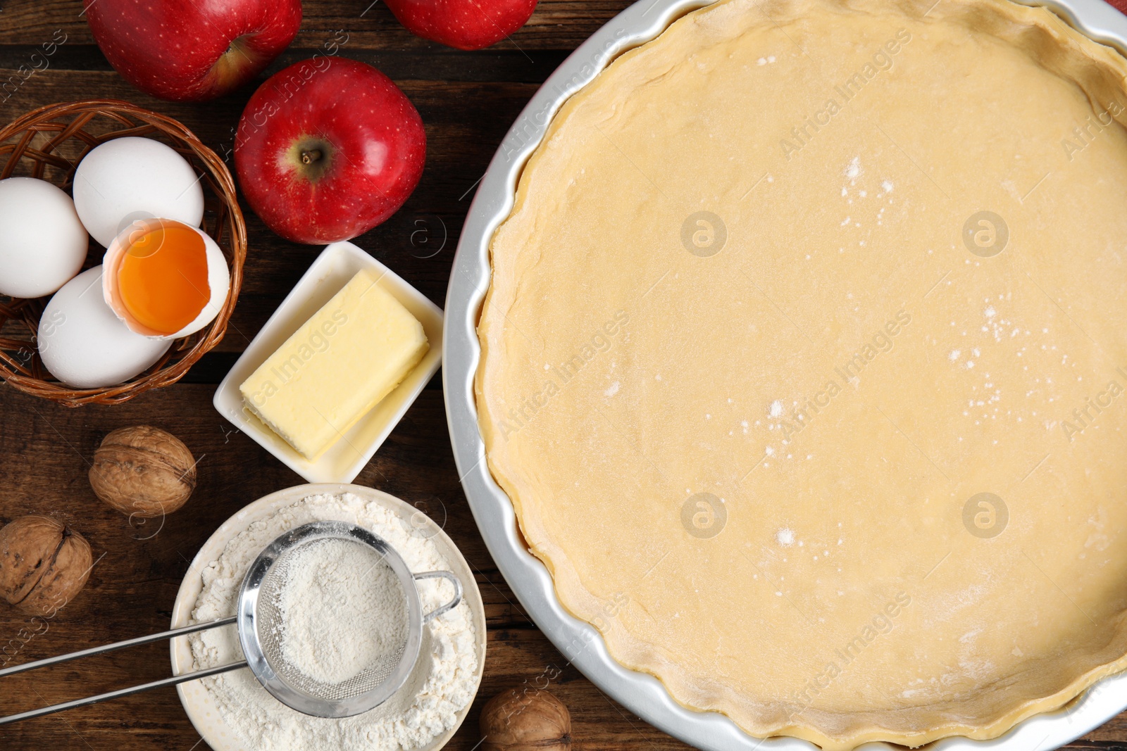 Photo of Raw dough and ingredients for traditional English apple pie on wooden table, flat lay