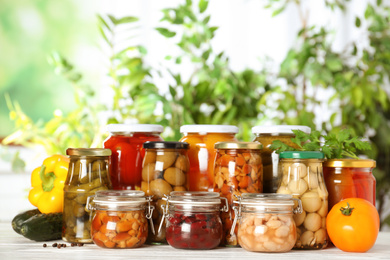 Photo of Glass jars of different pickled vegetables on white wooden table