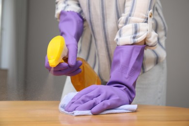 Photo of Woman cleaning wooden table with detergent and rag indoors, closeup