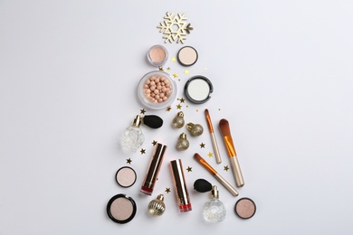 Photo of Christmas tree shape of decorative cosmetic products on light background, flat lay.  Winter care