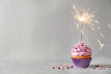 Photo of Delicious birthday cupcake with sparkler on grey background