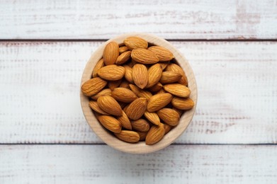 Photo of Tasty almonds in bowl on white wooden table, top view