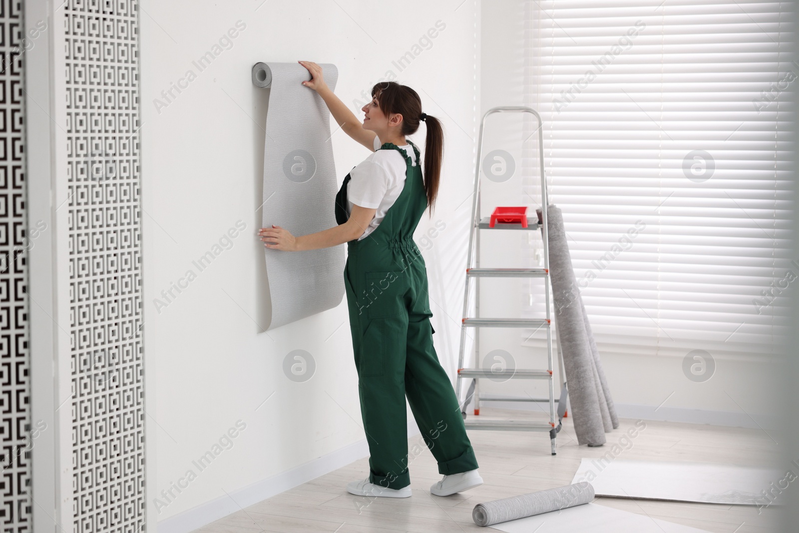 Photo of Woman hanging stylish gray wallpaper in room