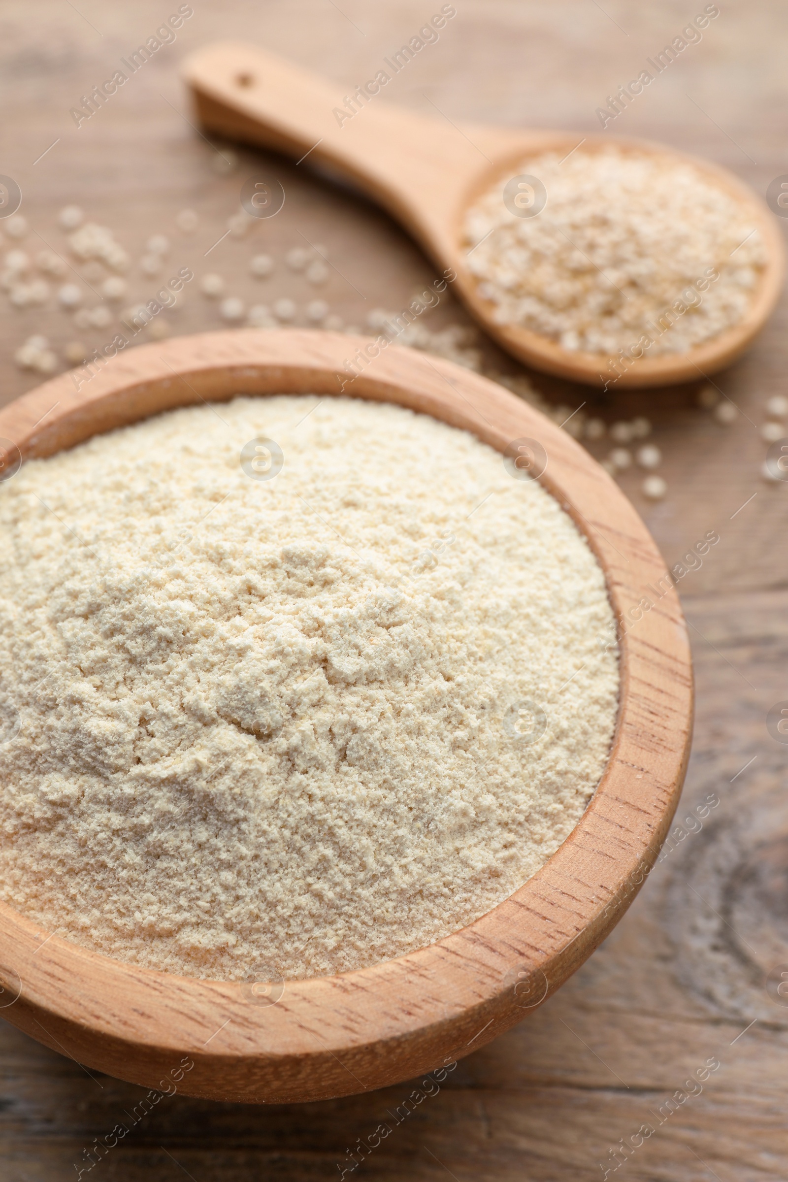 Photo of Quinoa flour in bowl and spoon with seeds on wooden table