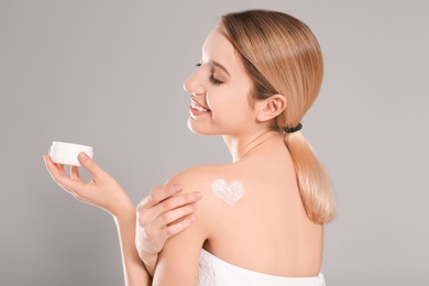 Young woman with jar of body cream on color background