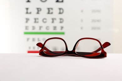 Photo of Glasses with corrective lenses on table against eye chart
