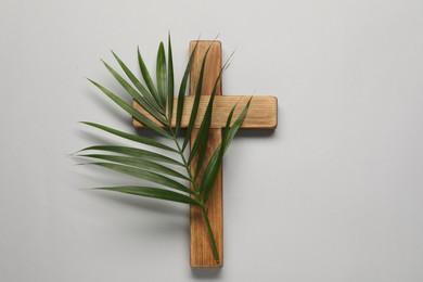 Photo of Wooden cross and palm leaf on light grey background, top view. Easter attributes