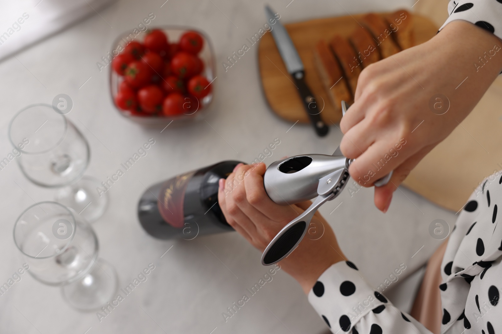 Photo of Romantic dinner. Woman opening wine bottle with corkscrew at table, top view