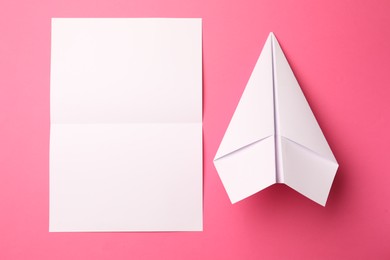 Photo of Handmade white plane and folded piece of paper on pink background, flat lay