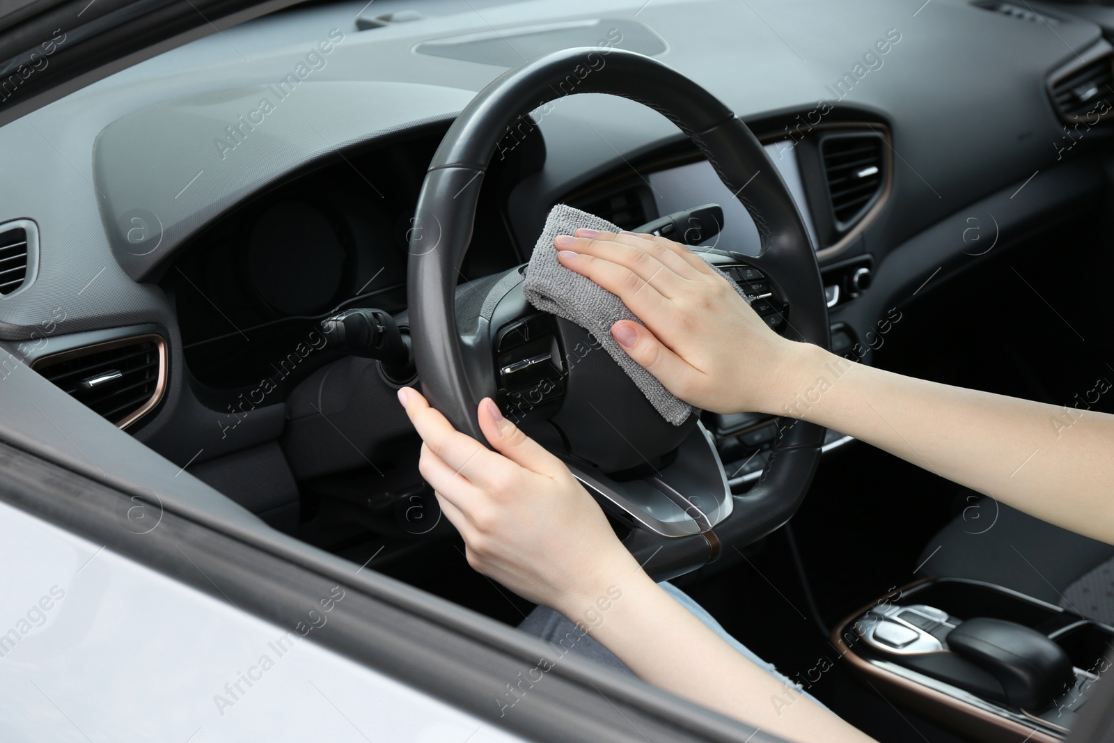 Photo of Woman cleaning steering wheel with rag in car, closeup