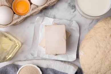 Yeast and ingredients for dough on white marble table, flat lay