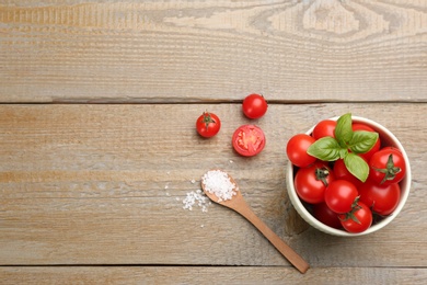 Fresh cherry tomatoes, sea salt and basil leaves on wooden table, flat lay. Space for text