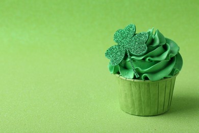 Photo of St. Patrick's day party. Tasty cupcake with clover leaf topper and cream on green background. Space for text