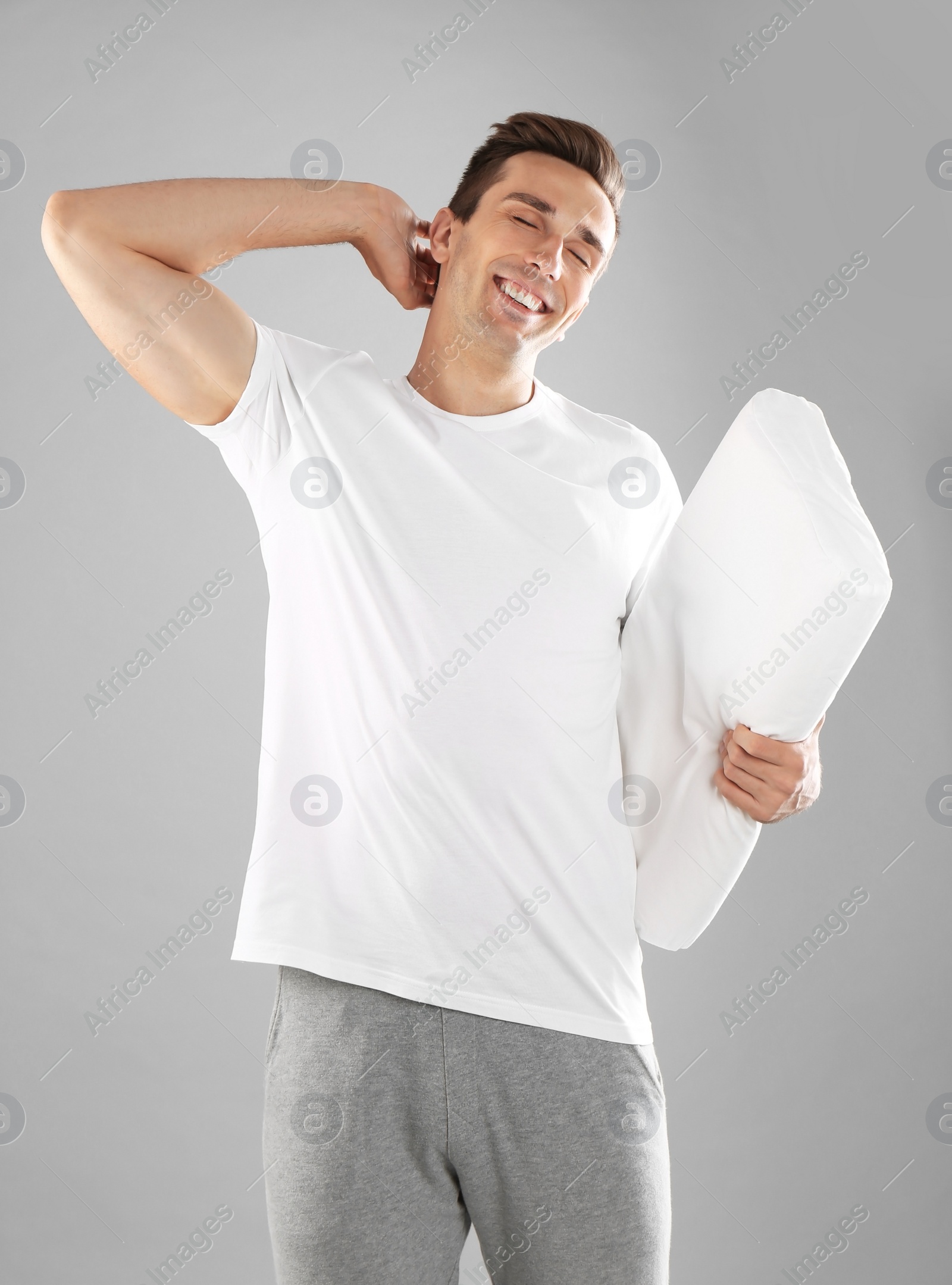 Photo of Young man in pajamas with pillow on gray background