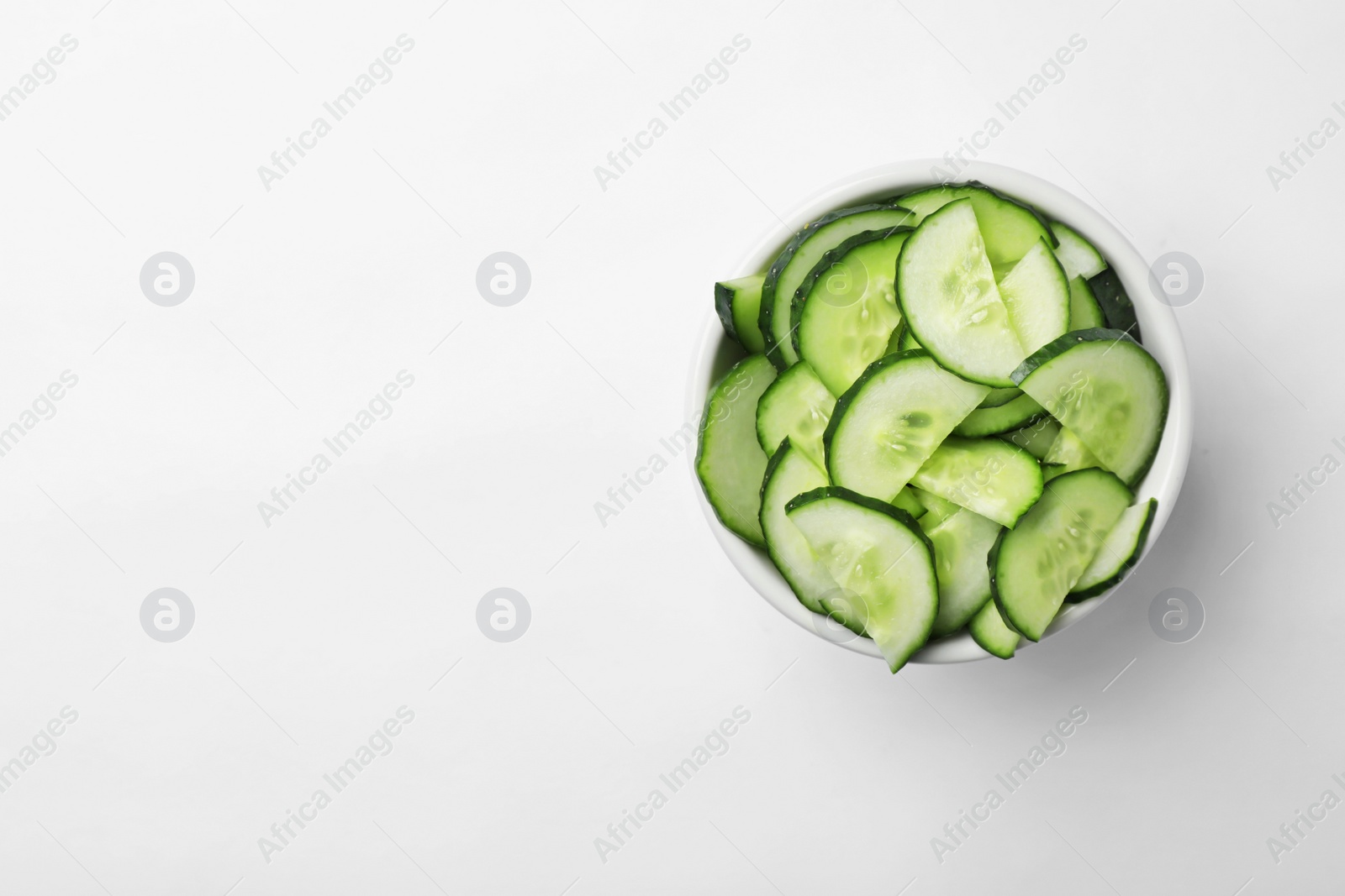 Photo of Bowl with slices of ripe cucumber on white background, top view