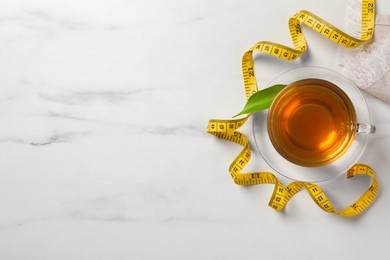 Flat lay composition with herbal diet tea and measuring tape on white marble table, space for text. Weight loss concept