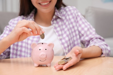 Happy woman putting coin into piggy bank at home