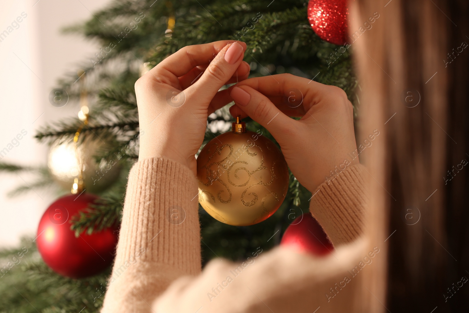 Photo of Woman decorating Christmas tree with beautiful golden bauble, closeup