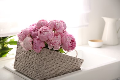 Basket with beautiful pink peonies in kitchen