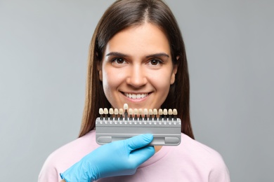 Photo of Doctor checking young woman's teeth color on light grey background. Cosmetic dentistry
