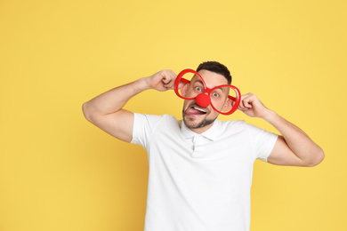 Photo of Funny man with clown nose and large glasses on yellow background. April fool's day