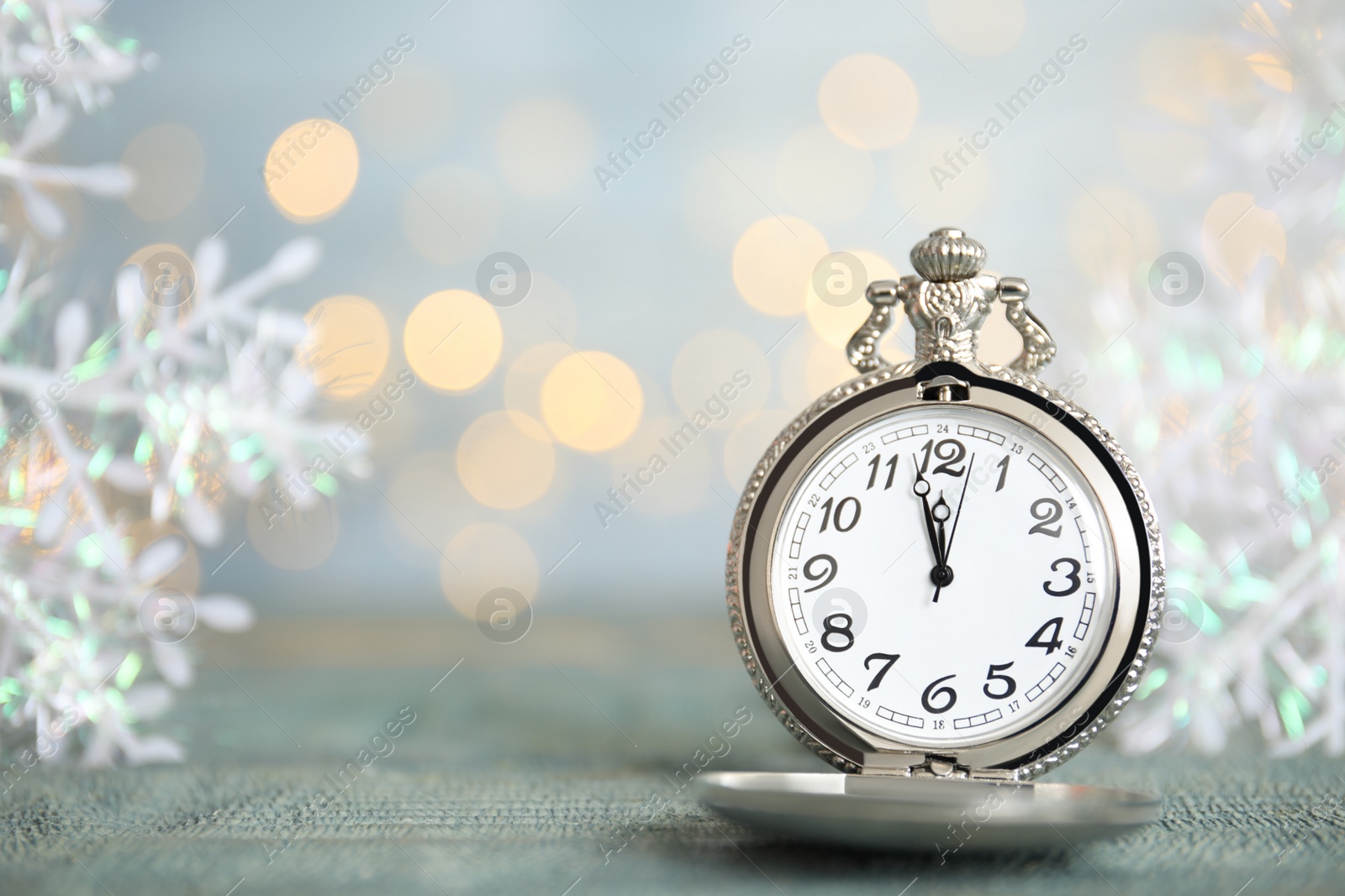 Photo of Pocket watch and festive decor on table against blurred lights, space for text. New Year countdown