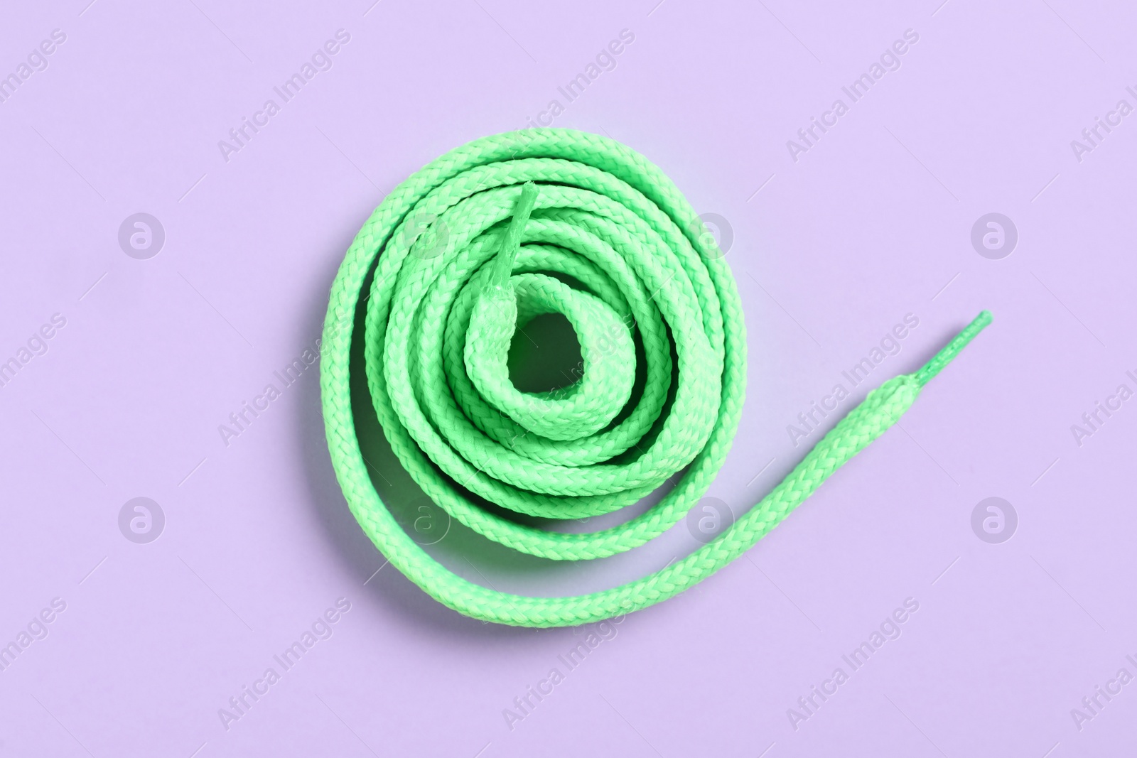 Photo of Green shoelace on lilac background, top view