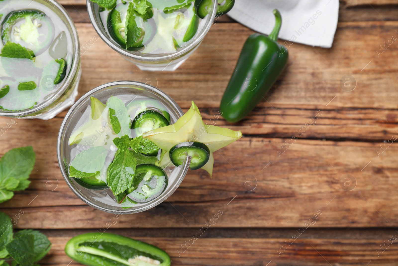 Photo of Glasses of spicy cocktail with jalapeno, carambola and mint on wooden table, flat lay. Space for text