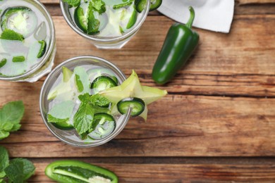 Glasses of spicy cocktail with jalapeno, carambola and mint on wooden table, flat lay. Space for text