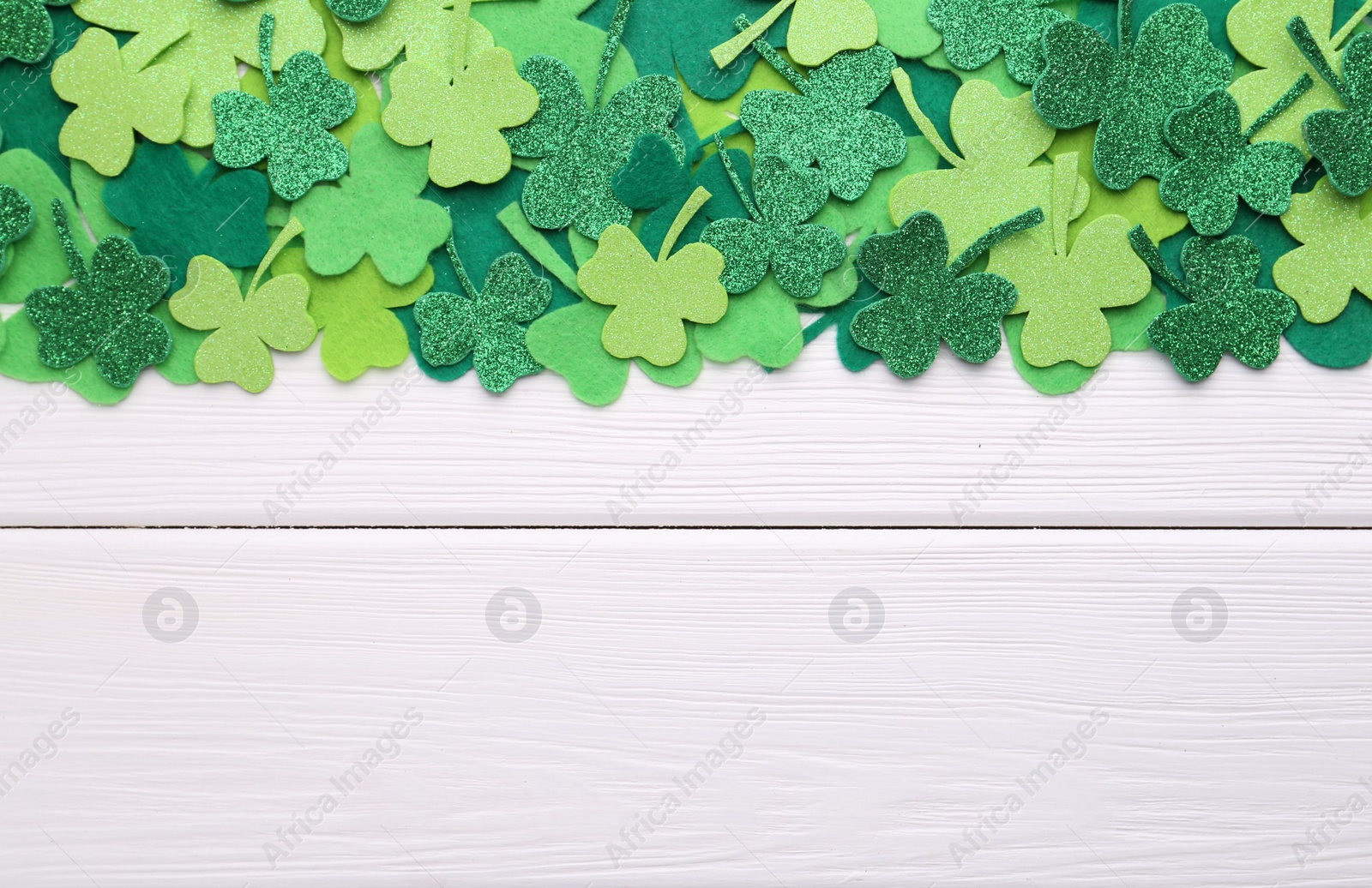 Photo of St. Patrick's day. Decorative green clover leaves on white wooden table, flat lay. Space for text