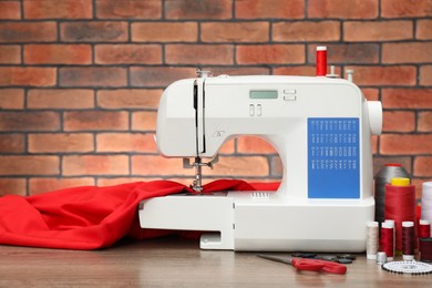 Sewing machine with fabric and craft accessories on wooden table against brick wall