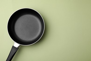 Photo of One frying pan on light olive background, top view. Space for text