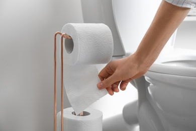 Photo of Woman taking toilet paper from roll holder in bathroom, closeup