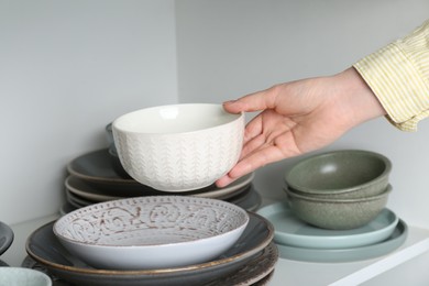 Photo of Woman taking ceramic bowl from shelf, closeup