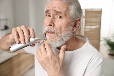 Photo of Senior man trimming mustache with electric trimmer in bathroom