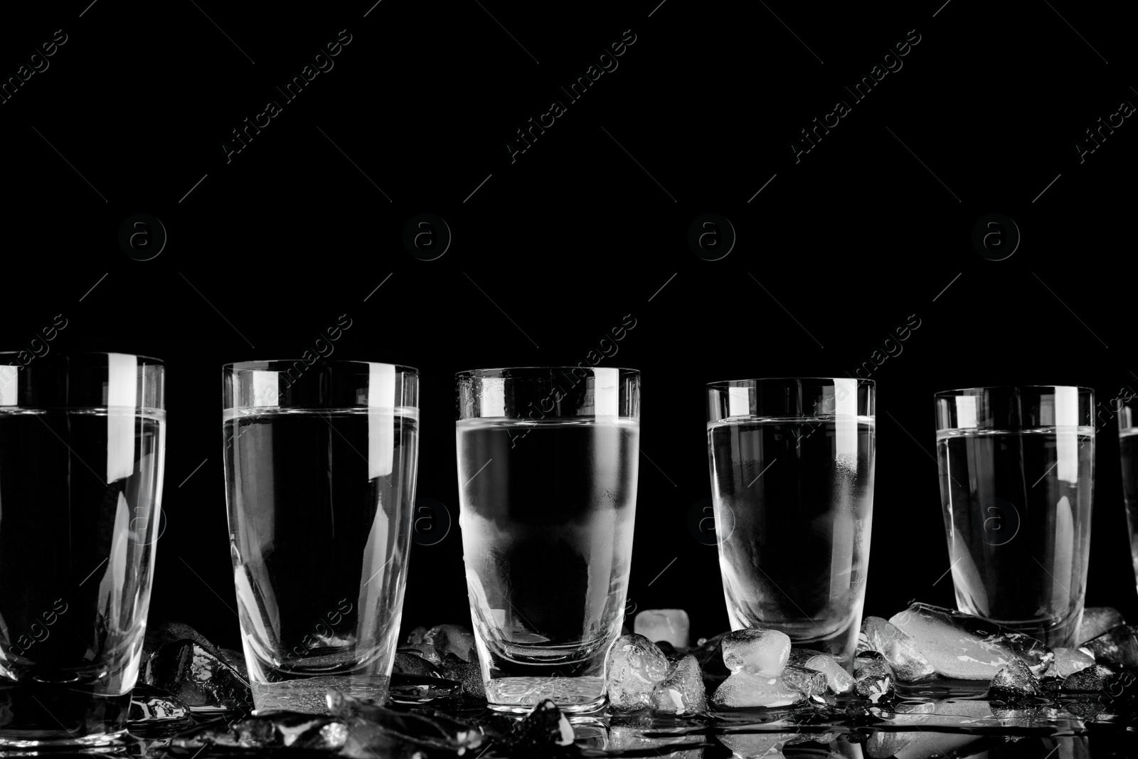 Photo of Vodka in shot glasses and ice on black background